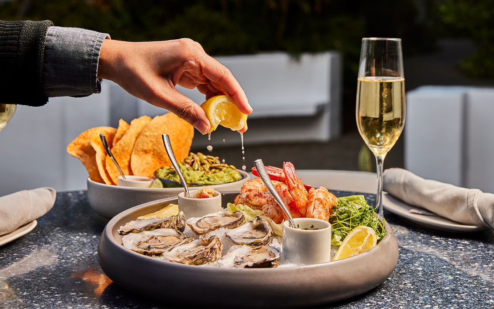 Plated gourmet dish at Cavatina restaurant in the Sunset Marquis, featuring artfully arranged, vibrant ingredients served outdoors on a dark table set amidst garden greenery.